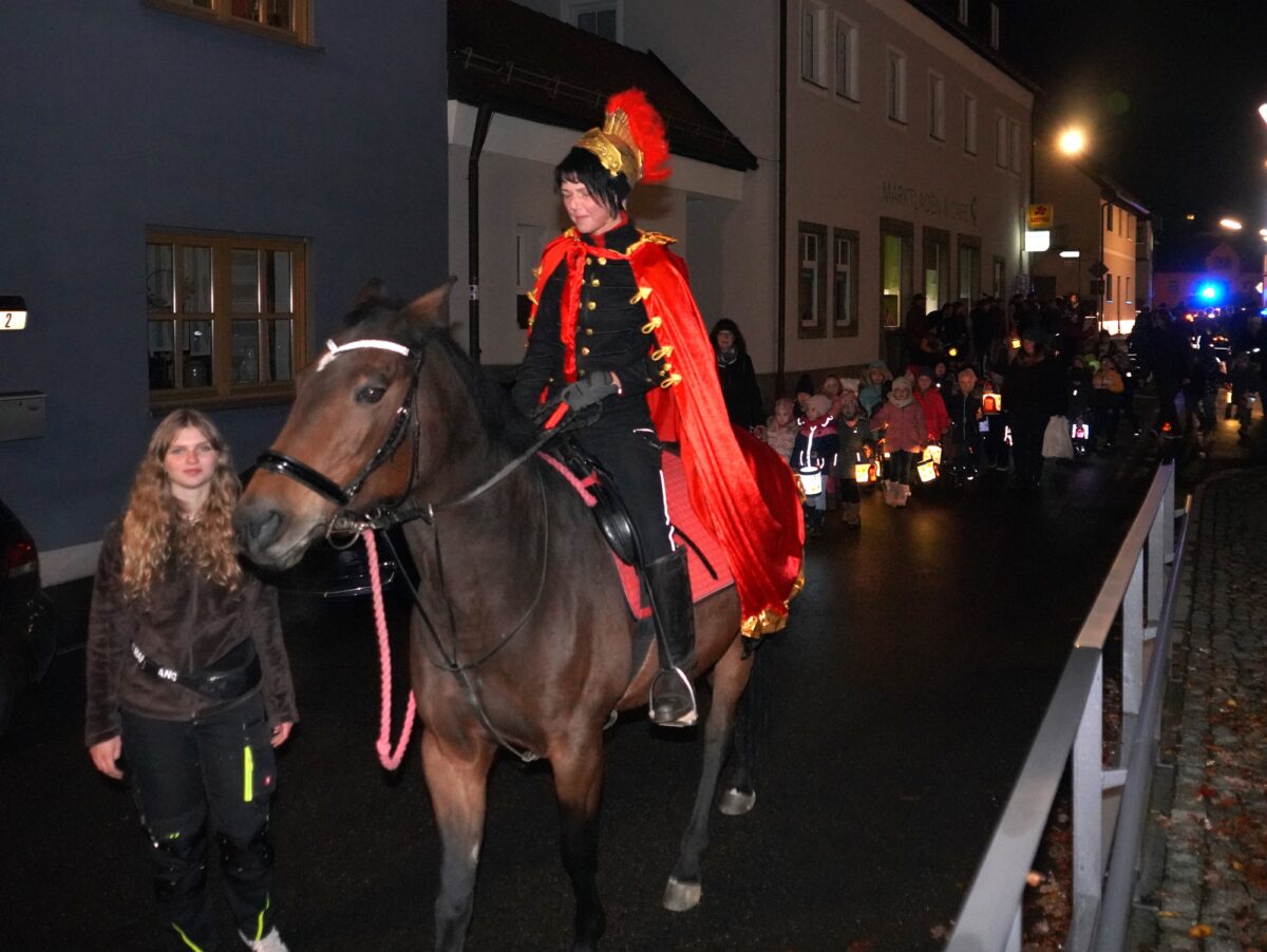 Bild (fvo) Mit stoischer Gelassenheit marschiert das Pferd „Lady Toskana“ mit ihrer Reiterin Rebecca Bergler beim Martinszug von der Pfarrkirche zur Kita. Foto: Franz Völkl
